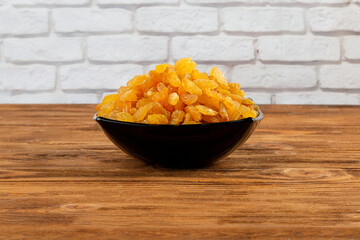 Raisins in a dark plate, on a wooden table against a brick wall.