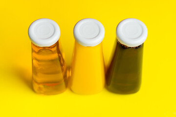 Bottles with yellow and red liquid halthy beverage on yellow background. Orange apple cherry juice