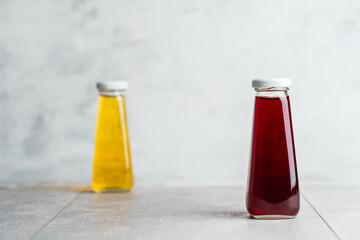 Bottles with yellow and red liquid halthy beverage on gray background. Orange and cherry juice