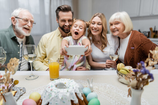excited girl with open mouth taking selfie on smartphone during easter dinner with family.