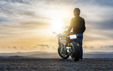 Male biker with his motorbike (motorcycle) watching the sunset and enjoying freedom and active...