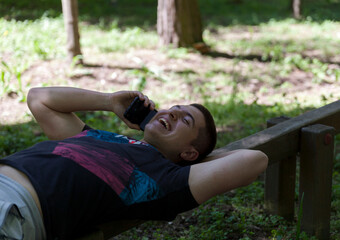 Handsome young smiling man,talking on mobile phone ,lying on a wooden beam in the woods.