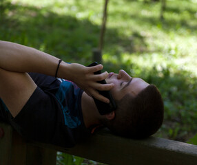 Handsome young man,talking on mobile phone ,lying on a wooden beam in the woods.