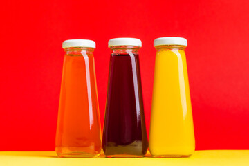 Bottles with yellow and red liquid halthy beverage on yellow and red background. Orange apple cherry