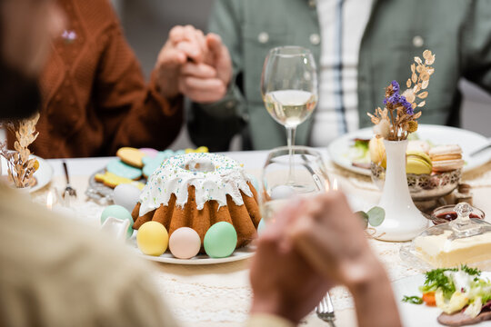 cropped view of family holding hands near easter cake and painted eggs on table.