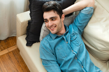 Young handsome man is relaxing on the sofa at home and thinking about the future. Caucasian millennial lies on the sofa, relaxes and looks away.