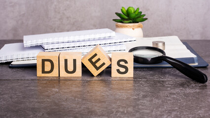 the word Dues is written on wooden cubes on a gray background. close-up of wooden elements, magnifying glass, paper documents