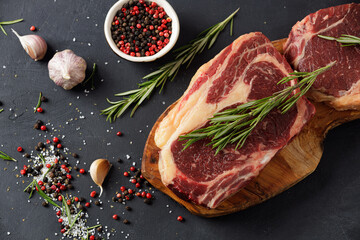 Raw beef steak on a cutting board with rosemary, garlic and spices.