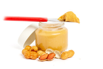 Glass and knife with peanut butter on white background with peanuts around