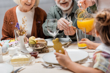 cropped view of woman pouring orange juice near family having easter dinner.