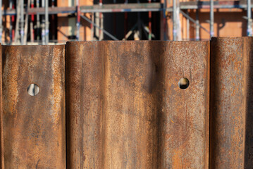 Detail of a rusty sheet piling standing in front of a building that is still under construction