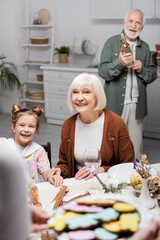 senior man opening wine bottle near family celebrating easter at home.