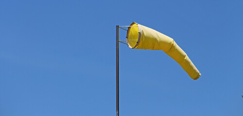 Yellow windsock on a pole with a blue sky background. - obrazy, fototapety, plakaty