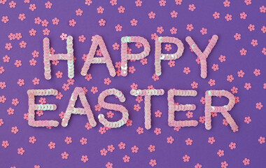 Inscription of "Happy Easter" embroidered with pink sequins on purple textured background with scattered random sequins in form of flowers