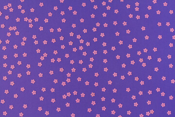 Scattered random pink sequins in form of flowers on purple textured background