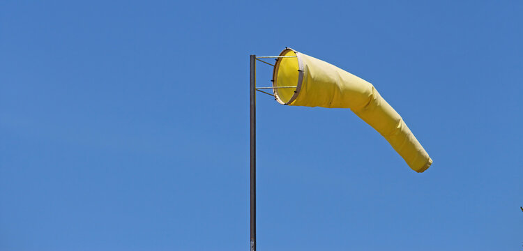 Yellow windsock on a pole with a blue sky background.