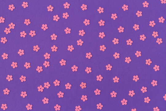Scattered random pink sequins in form of flowers on purple textured background