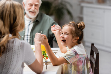 excited girl holding hands with blurred mom and granddad during easter dinner.