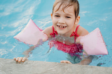 a funny little girl swims and plays in inflatable armbands in a pool