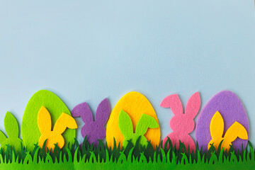 Easter hunt concept. Colorful Easter bunnies and eggs in grass on blue background, top view with space for text. Happy Easter! Pink, yellow, purple artificial bunny and egg decor