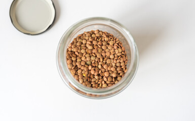 High angle closeup of brown lentils in glass jar on white background (selective focus)