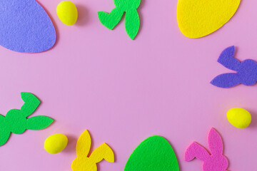 Colorful Easter bunnies and eggs frame on pink background, flat lay with space for text. Happy Easter! Purple, pink, yellow artificial bunny and egg decor. Creative Easter hunt concept