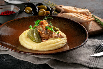 Mashed potatoes with beef stew in sauce, pickles and fried onions. Meat dish served on a plate