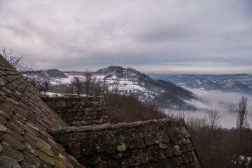 Old vintage tile rooftop on village house, against scenic view of snow covered mountains and forest in Serbia.