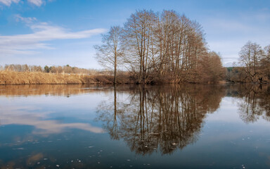 Spring landscape in early spring. River, trees without leaves, reflection in the water