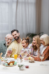 smiling man showing smartphone to amazed family during easter dinner.