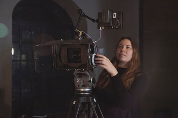 A young female director of photography at work behind a movie camera on a film set for a movie, commercial or broadcast - obrazy, fototapety, plakaty
