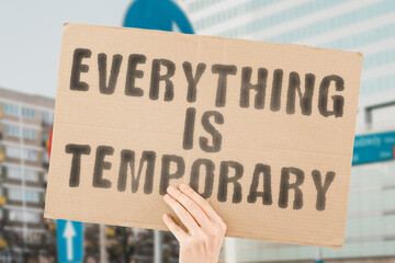 The phrase " Everything is temporary " on a banner in men's hand with blurred background. Goal. Genius. Bad. Risky. Fake. Facts. Hour. Life. Policy. Idea. Way. Move. Effect. Job. Plan