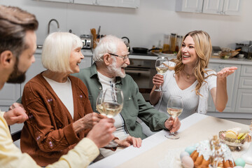 cheerful woman with wine glass pointing with hand during easter dinner with family.