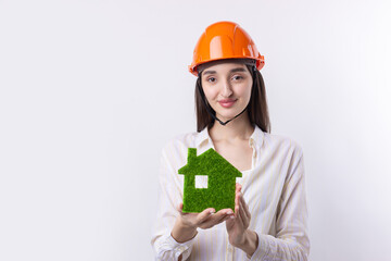 A young girl architect in a construction helmet demonstrates a model of a green house. Sale of ecological real estate.