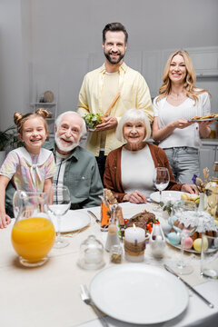 happy family smiling at camera near table served with easter dinner.