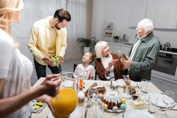 men holding bottle of wine and vegetable salad during easter dinner with family.
