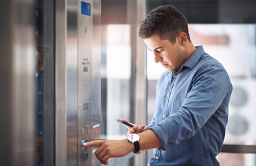 Fototapeta premium Hes heading straight to the top. Shot of a young businessman using a cellphone while pushing a button in an elevator.