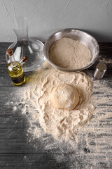 The process of preparing dough in the kitchen. Kneading dough for baking bakery products or pizza. Water, flour scattered on the table, oil and salt on a dark wooden table. Top view, selective focus.