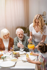 smiling woman pouring orange juice while family having easter dinner at home.