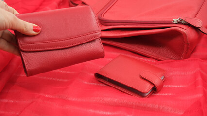 Red wallets and purse on red background. A woman's hand with red nail polish is holding a red wallet