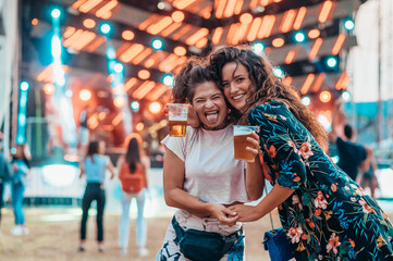 Two beautiful friends drinking beer and having fun on a music festival