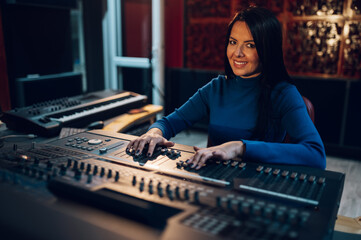 Woman music producer working on a mixing soundboard in a studio.