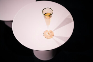 A luxury golden glass with sparkling champagne on white circle table against black background.
