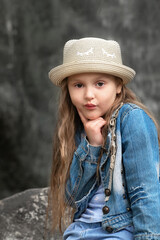 Portrait of a little beautiful preschool girl with long wavy hair in a straw hat on a warm summer walk in the park