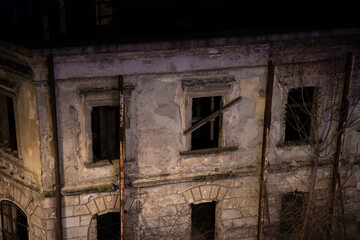 Fototapeta na wymiar Old abandoned house at night in Belgrade city center. Broken windows boarded up with wooden planks and facade of old decaying house ruins.