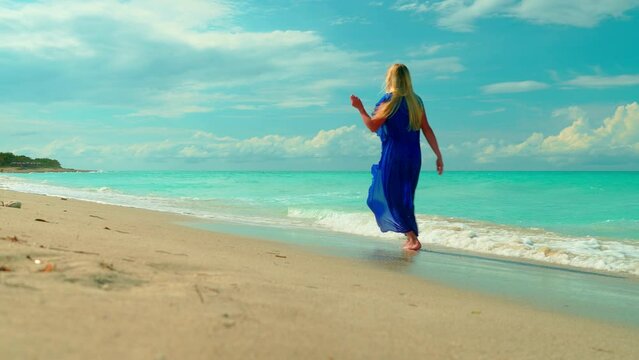 girl in blue dress run along the shore of the blue sea.