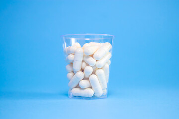 Capsules in transparent plastic cup on blue background. Pharmaceutics, capsule pills.