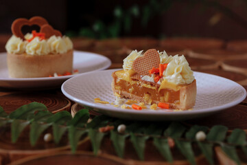 dessert, cheesecake with mango and passion fruit in the form of brownies with mousse on top. Decorated with cookies in the form of a heart. On a wooden table in a white plate