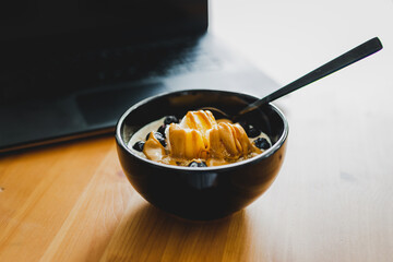 eating mango blueberries oatmeal while working from home on a laptop, remote working or lunch at the office.