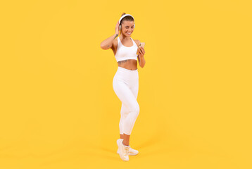 sport woman with headphones and smartphone on yellow background. full length